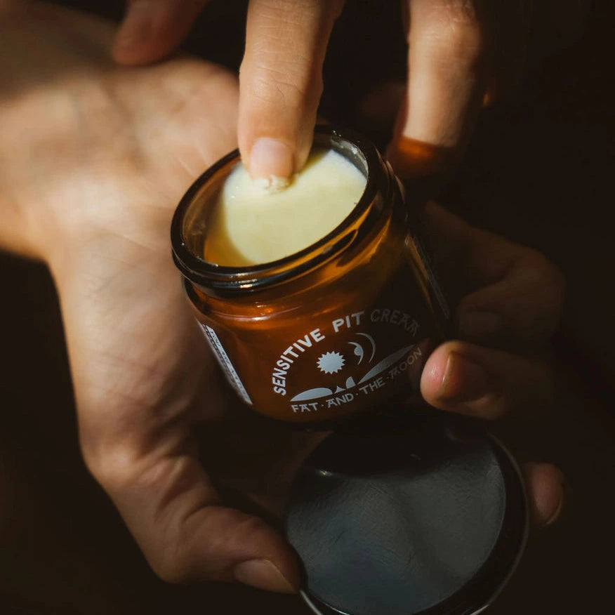 Person applying deodorant cream from a jar labeled 'Sensitive Pit Cream' with a dark background