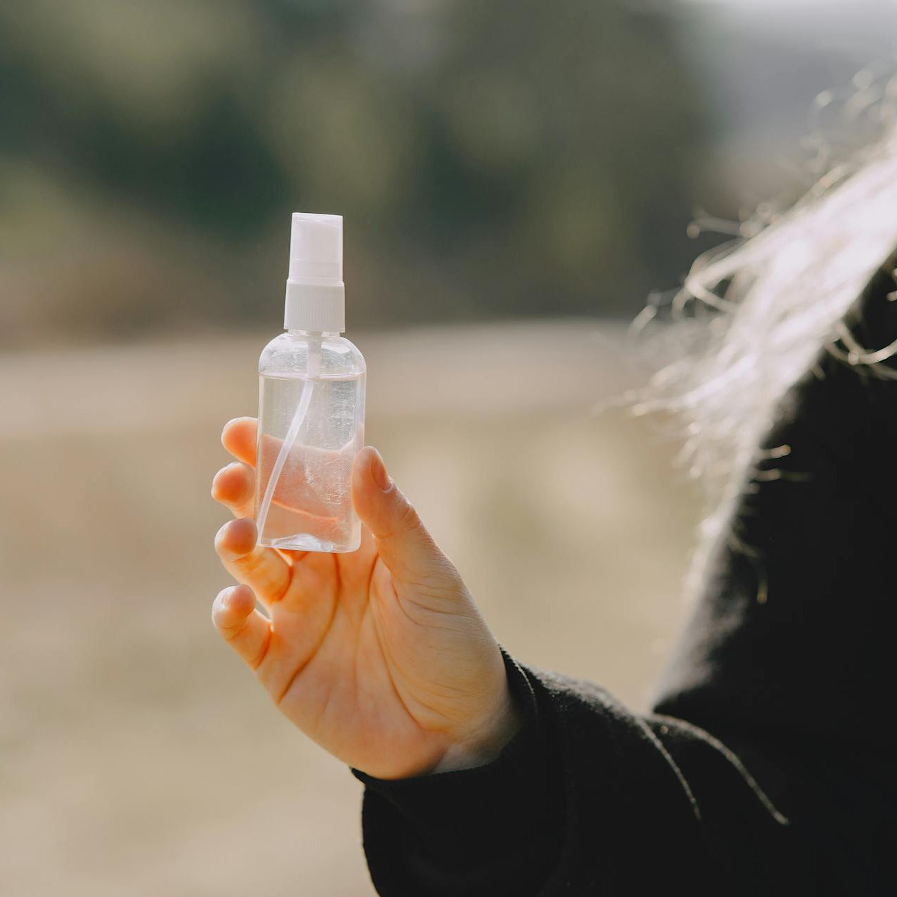 Hand holding a small spray bottle outdoors with a blurred natural background