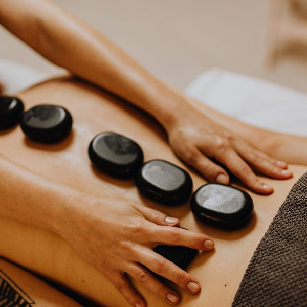 A person giving a back massage with massage stones, representing the raffle item one hour massage offered by Diosa Massage
