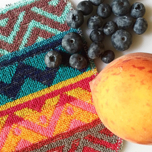 A colorful EuroScrubby next to a peach and a cluster of blueberries.