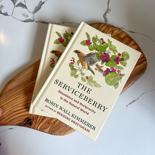 Book titled 'The Serviceberry' on a wooden surface with a marble background