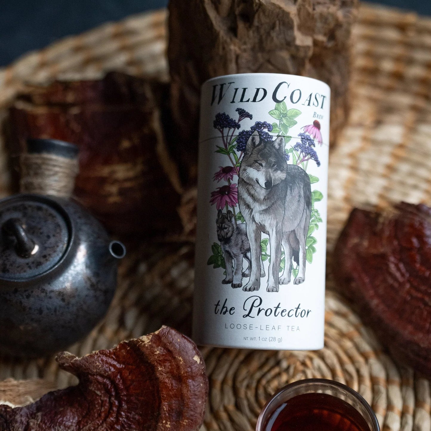 Bottle of Wild Coast Tea with a label featuring wolves on a woven mat with wood and a teapot.