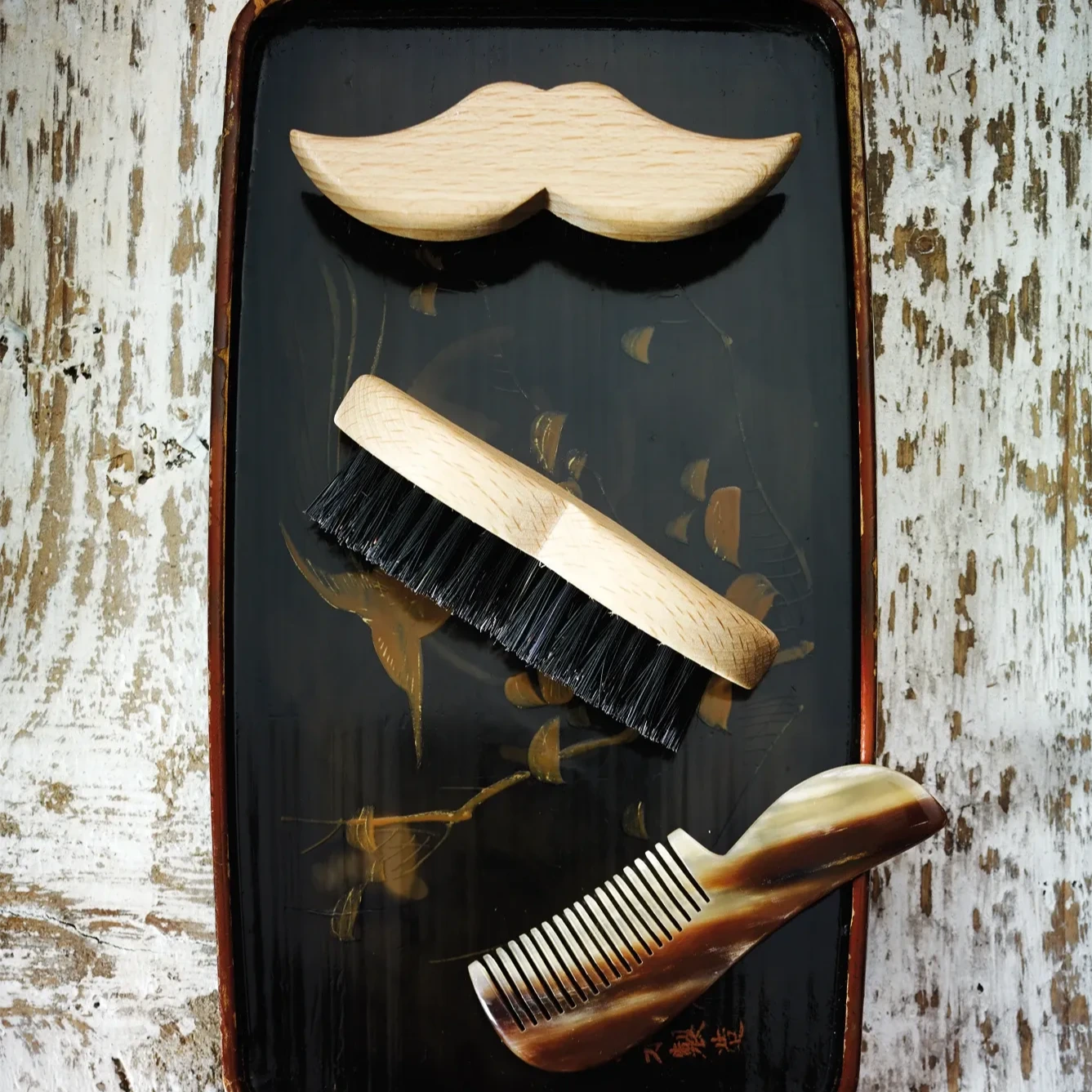Beard grooming tools on a dark tray with a mustache design.