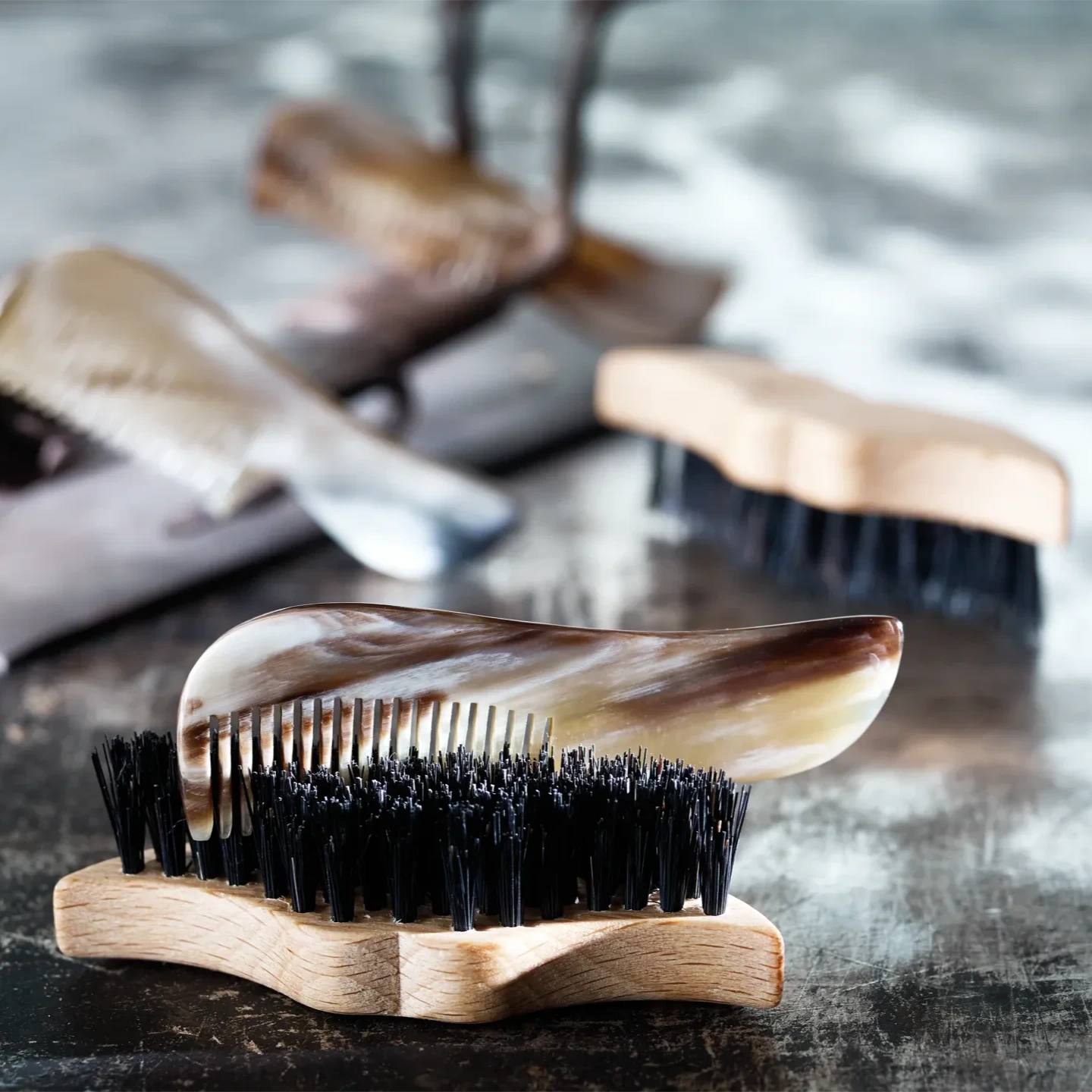 A wooden beard/mustache brush with black bristles, displayed on a surface, with other brushes in the background.