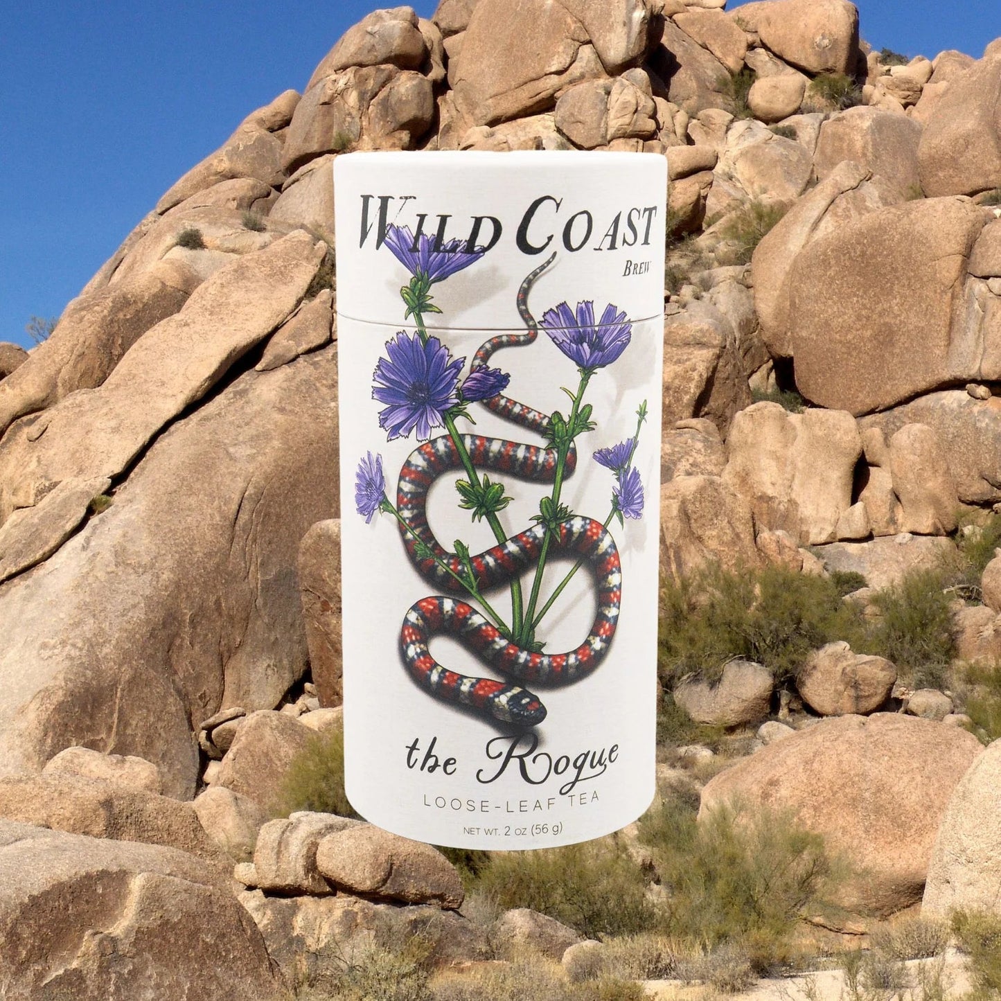 Canister of Wild Coast Tea with a snake and flower design in front of rocky desert landscape