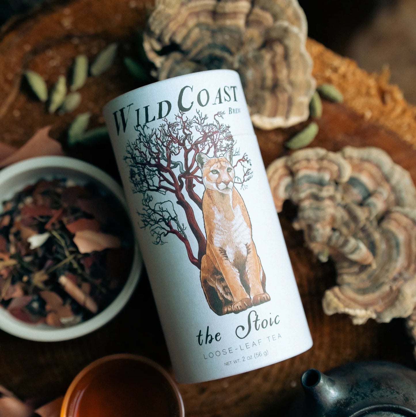 Tea canister labeled 'Wild Coast' with a teacup and tea leaves on a wooden surface.