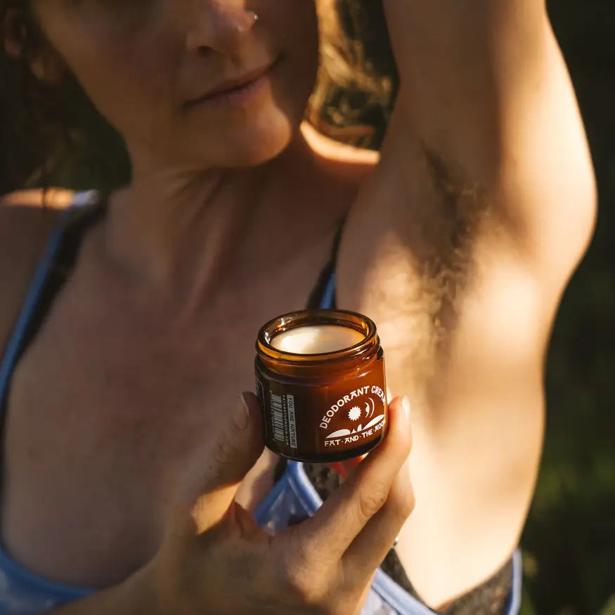 Person applying deodorant cream to armpit with a jar of the product held in hand.