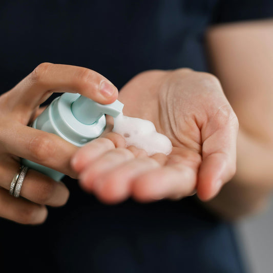 Person applying a foaming hand soap from a small container into their palm.