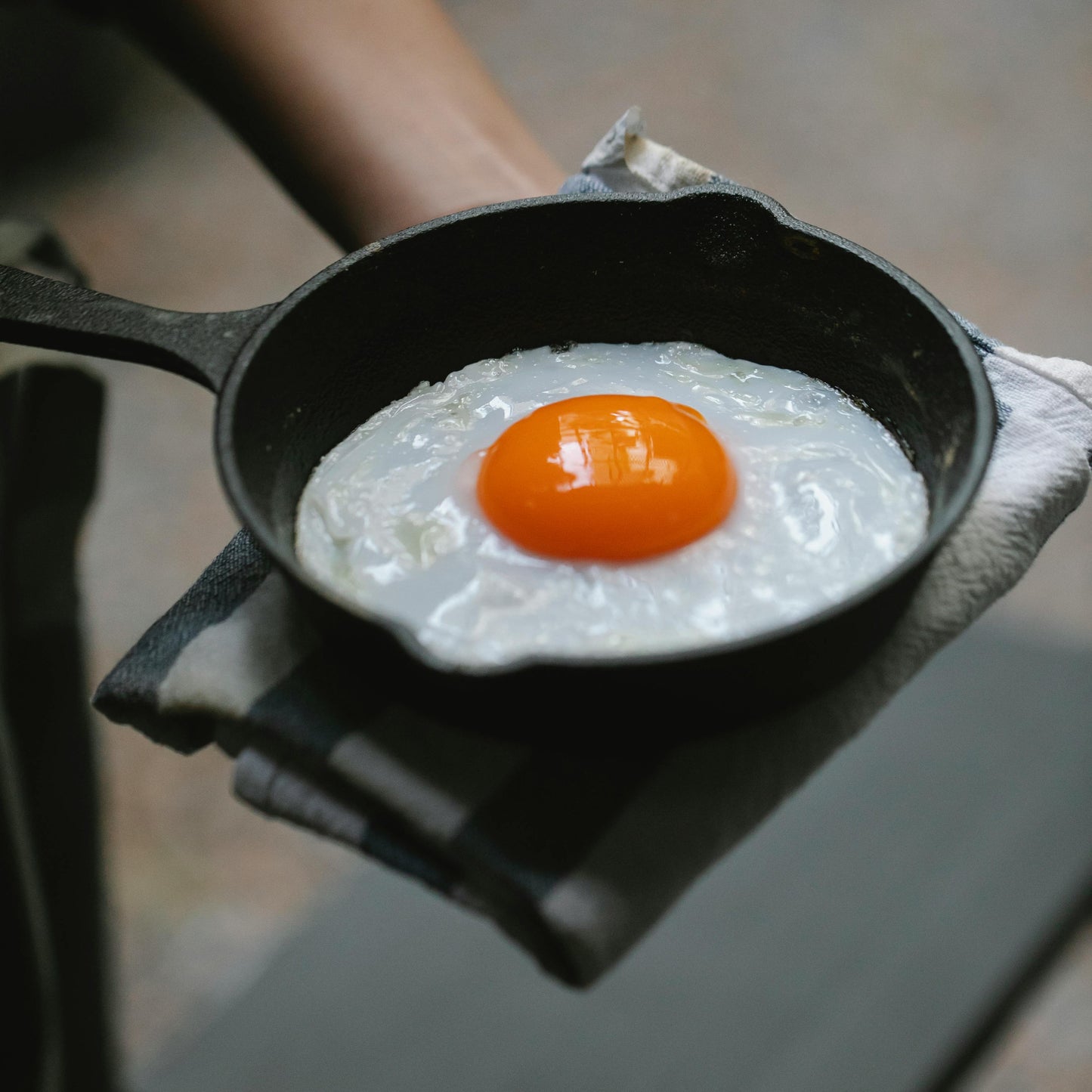 Fried egg in a small cast iron skillet held by a person on a wooden surface.