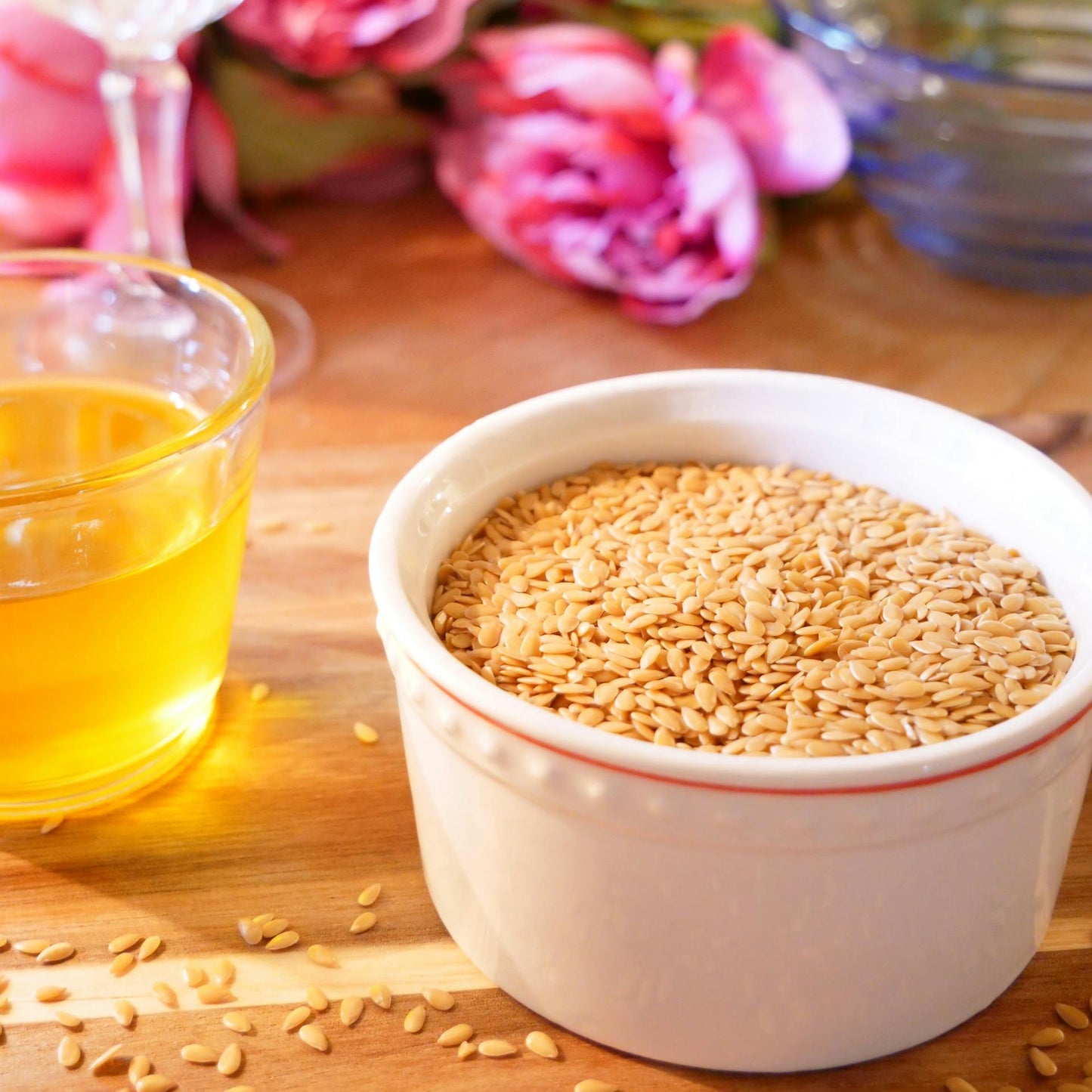 White bowl filled with sesame seeds on a wooden surface with pink flowers in the background.