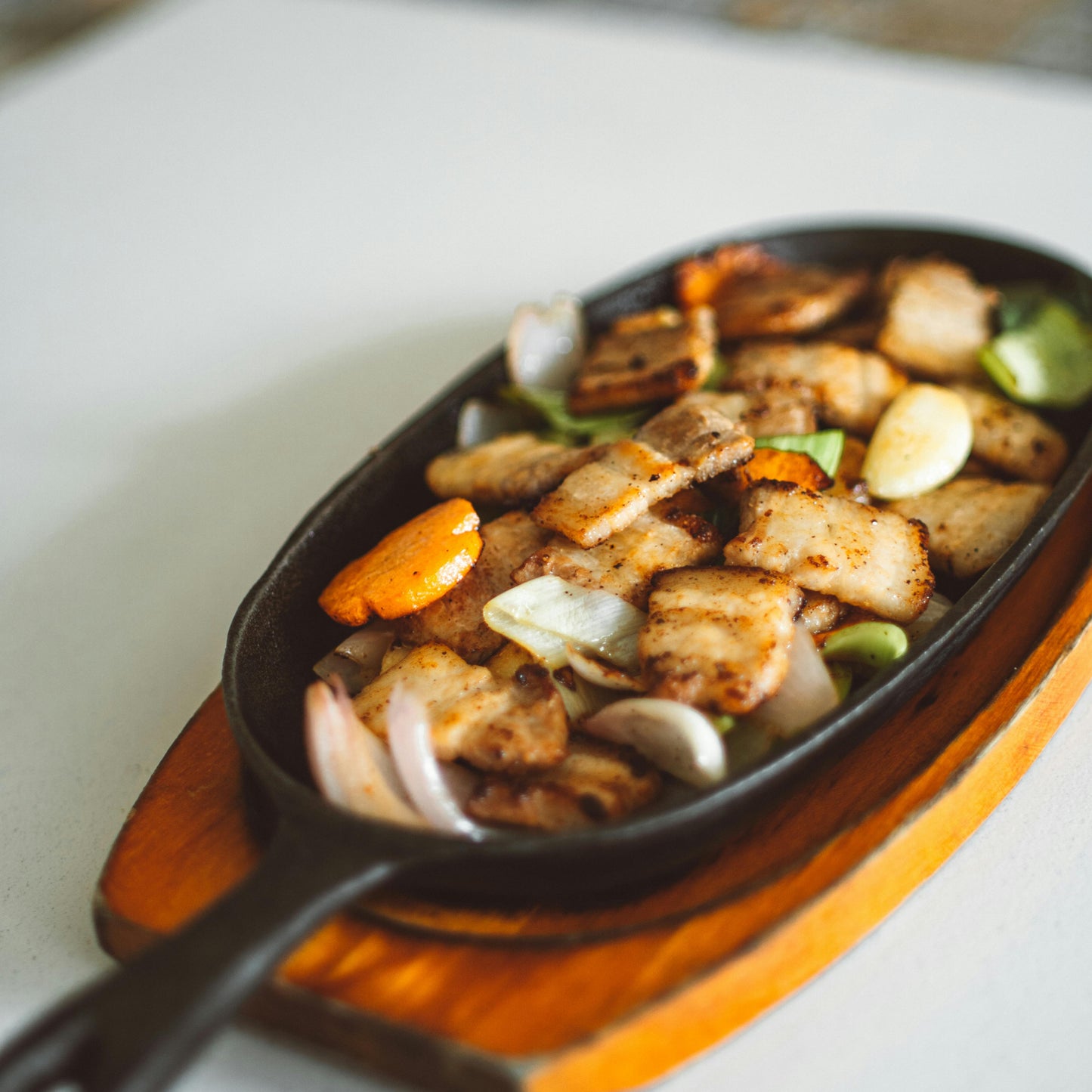 Fried chicken with vegetables in a cast iron skillet on a wooden board.