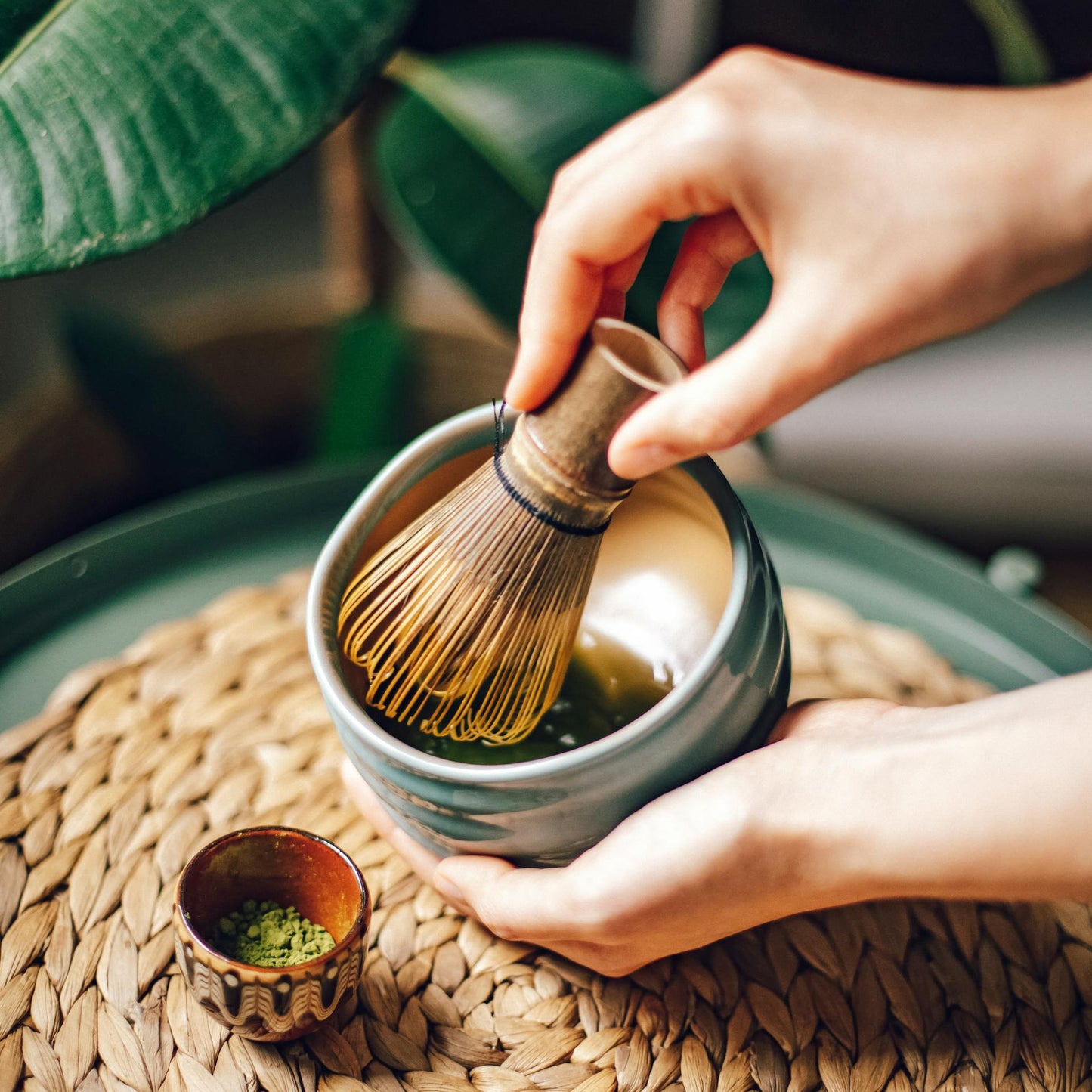 Person preparing matcha tea with a whisk on a woven mat