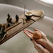 Person holding a loofah sponge in front of a bath bomb with various bath items on a tray.